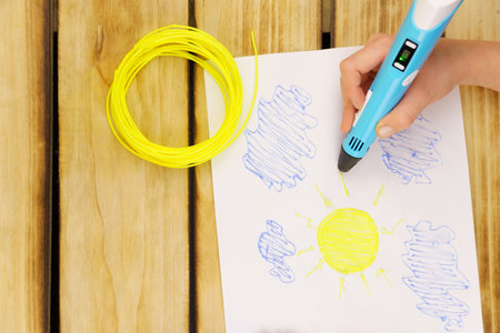 The child's hand holds a 3D pen and creates the sky, blue clouds and yellow sun. Creativity, future...