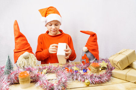 A boy dressed as a gnome opens a box with a Christmas present. Scandinavian gnomes. Christmas holidaysの写真素材
