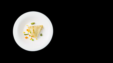 A thin pancake with a healthy filling on a white plate, over a black background with copy space. Corn, peas, asparagus and carrots are wrapped in a pancake. Healthy and balanced nutrition.の写真素材