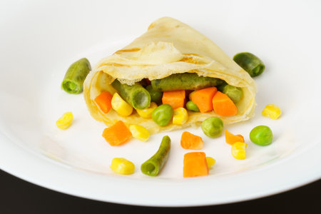 Pieces of vegetables are wrapped in a thin pancake on a white plate.