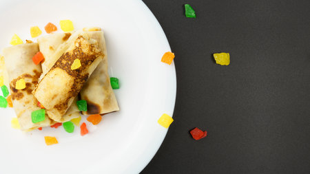 Top view of white plate with thin pancakes stuffed with candied fruits on black background with copy space.の写真素材