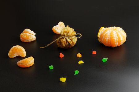 One thin ruddy pancake with filling, wrapped in a bag and tied with thread, next to candied fruits and tangerines. Pancake on a black background. Pancake week. Shrovetide for breakfast and carnival. Homemade baking.の写真素材