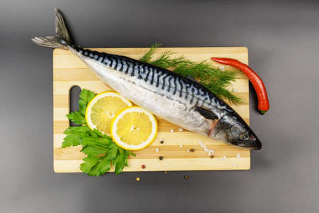 Raw mackerel on a wooden cutting board with spices, herbs and lemon on a black background. View from aboveの写真素材