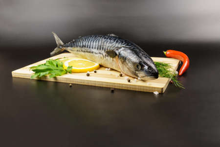 Fresh mackerel on a cutting board surrounded by lemon, dill, chili, parsley and spices on a black background with copy space.の写真素材