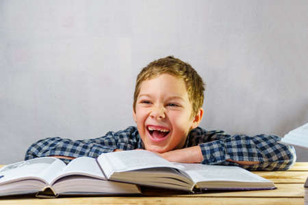 A happy schoolboy among open books. The child has no front teeth and is wearing a plaid shirt. Free...