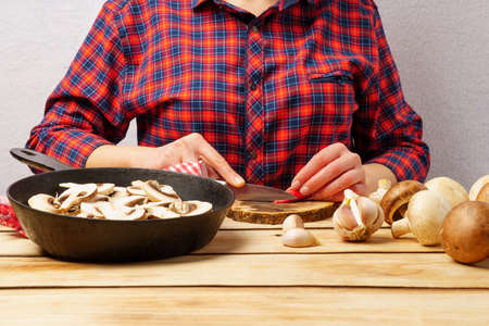 The girl cuts paprika. A girl in a red plaid shirt prepares mushrooms. Wood backgroundの写真素材