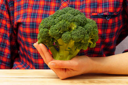 Close-up of broccoli in a female hand against the background of a plaid shirt. Healthy food