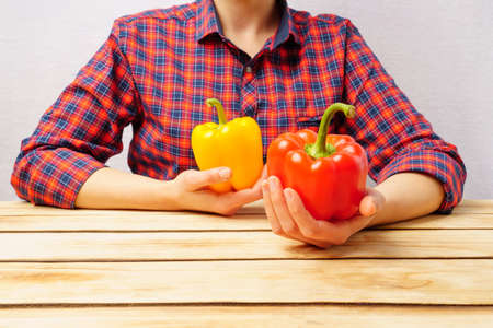 A woman holds a bell pepper in her hands. The girl is sitting at the table dressed in a checkered red shirt and holding ripe peppers.の写真素材