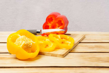 Juicy bell pepper cut into rings and a knife on a cutting board on a wooden background. Chopped...