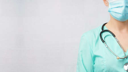 Close-up of a female doctor in a medical mask and green suit with a stethoscope. Gray background with copy spaceの写真素材
