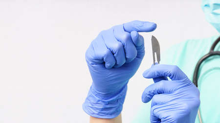Woman doctor in blue gloves holds scalpel in hand on white background with copy space
