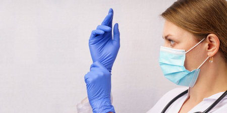 Female doctor wearing protective surgical gloves, face mask, and stethoscope on a white background.