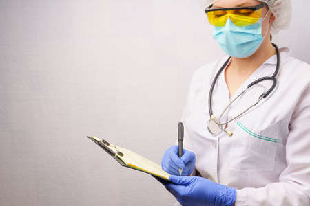 woman doctor fills out a patient's medical history form. gray background with copy spaceの写真素材