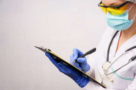 a doctor in a protective form fills out a patient registration form. gray background with copy space