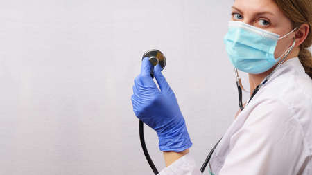 Woman doctor with stethoscope on white wall background