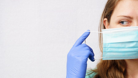 Close-up of woman putting on-taking off medical mask. white background with copy spaceの写真素材