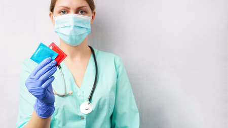 female doctor holds condoms in her hand. gray background, copy space. medicine and healthcare conceptの写真素材