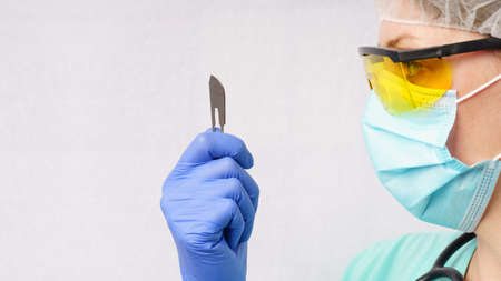 Portrait of a female surgeon wearing surgical scrubs, gloves and a cap, holding a surgical scalpel in her hand. White background with copy spaceの写真素材