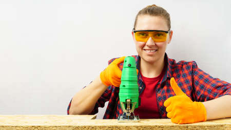 the process of sawing plywood with a jigsaw, a woman holds a tool in her hand, shows a thumb up, copy spaceの写真素材