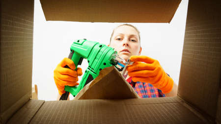 A woman looks into a cardboard box from the inside. Close-up photo of a woman peeking into a box and taking out an electric jigsawの写真素材