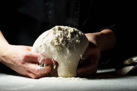 The dough in the hands of the cook among the flour on a dark background. copy space.