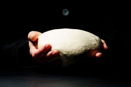 The cook holds the dough on a black background. Cooking concept.