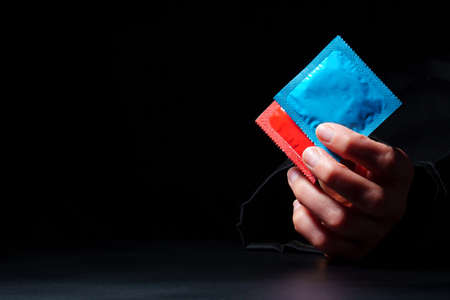 two colored condoms in hand on a dark background with copy space. safe sex concept. Infection...