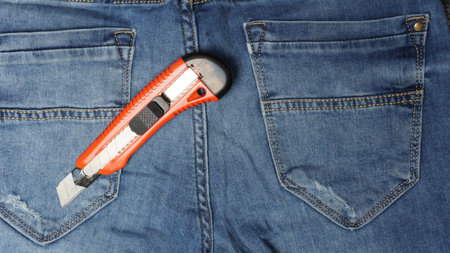 knife in blue denim pants. red utility knife on a denim background.の写真素材
