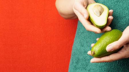 Young woman in green towel holding ripe beautiful halves of organic avocado avocado with bone. Girl...