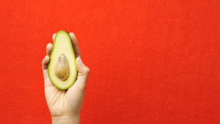 Avocado in hand. Woman holding ripe avocado on a red background. Healthy lifestyleの写真素材