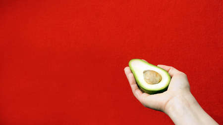 Avocado in hand on a red background, with copy space. A slice of avocado with a bone in the palm of your hand.の写真素材