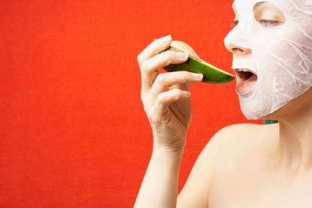 woman eating avocado over red background with copy space. Detox, cosmetology, diet, beautyの写真素材