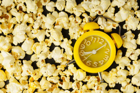 Popcorn and clock on a black background. The concept of movie time, vacation. Flat view.の写真素材