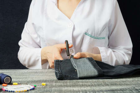 Woman hands cuts denim with scissors. A seamstress in a workshop is hemming jeans. Sewing processの写真素材