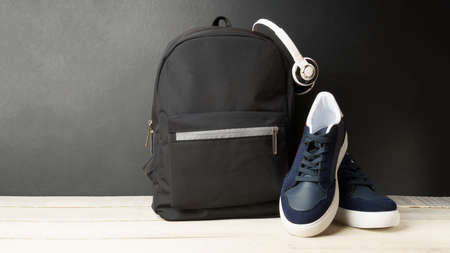 black backpack with headphones and sneakers on the background of a black wall, on a white wooden table. copy spaceの写真素材