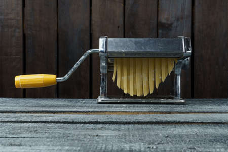 Cooking noodles on a pasta machine on dark wood backgroundの写真素材