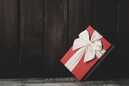 gift box on a dark wooden background. red box with white ribbon for holiday concept on black wooden...