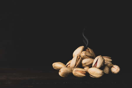 pistachios in smoke on a dark wooden background. close-up of steaming nuts