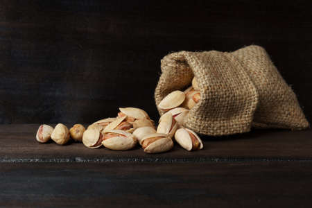 pistachios fall out of a bag, against a dark wooden background. fried salted pistachios. bannerの写真素材