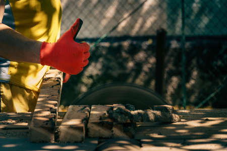 the carpenter raises his thumbs up to mark the class behind the circular saw. at the sawmill on a sunny day. bannerの写真素材