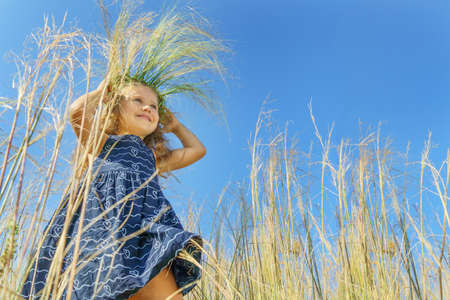 girl in a wreath on a background of blue sky. happy child, happy childhood.の写真素材