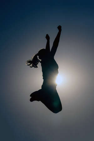 Silhouette of a beautiful woman jumping on the sunset sky.の写真素材