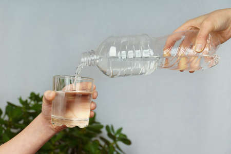 hand pours clean water from a bottle into a glass