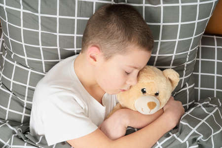 a boy with a teddy bear sleeps in a bed. cute baby sleepingの写真素材