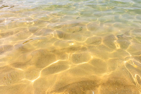 Ripples of water waves reflecting texture on a sandy beach bottomの写真素材