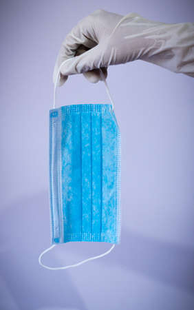 Medical face mask holding downside by gloved handの写真素材