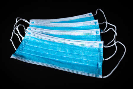 Four Surgical Face Masks lying on top of each in black background
