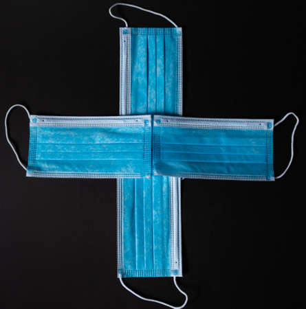 Four surgical face masks put together as a cross in black backgroundの写真素材