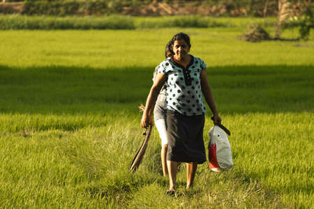 rural village woman walking with his daughter in the paddy filed caring things in both hands
