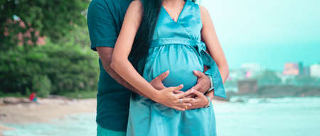Young parents expecting new baby holding mother's belly in both hands front close up photograph...